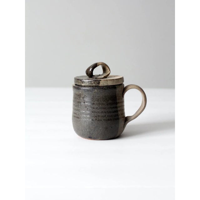 A vintage studio pottery lidded mug with hand-crafted ombré glaze transitioning from cream to charcoal. the softly...