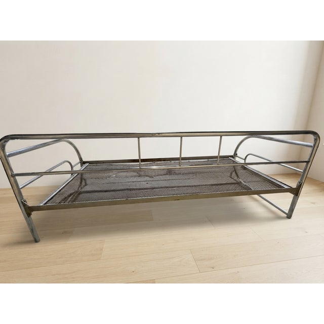 A distinctive vintage daybed frame with a chrome-plated tubular steel structure and woven metal mesh base. Its simple...