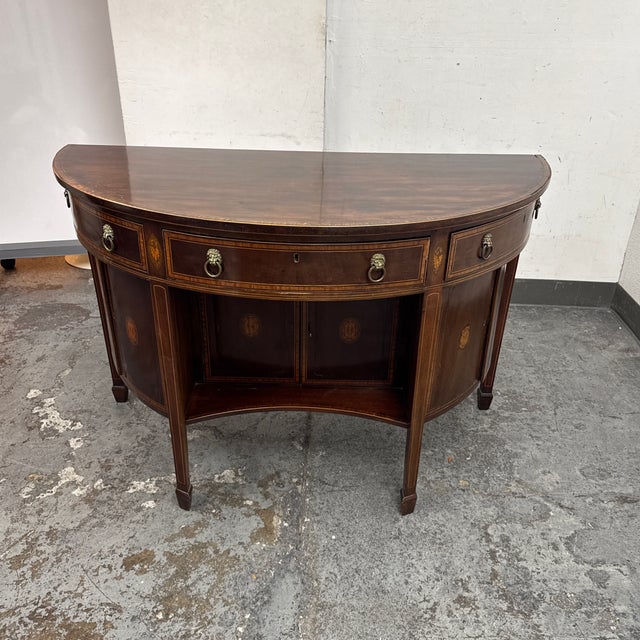 Design Plus Gallery presents an Antique Federal Style Inlaid Mahogany Sideboard. This demilune form sideboard is detailed...
