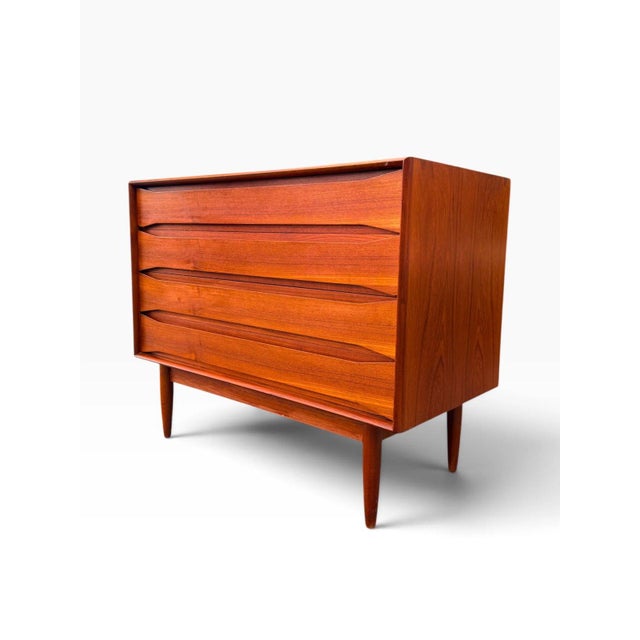 A Danish modern four-drawer dresser in richly figured teak, by Arne Vodder. Full-width sculpted pulls are carved directly...