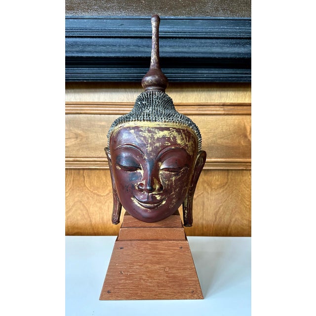 An antique lacquered and gilt wood buddha head on a custom wood stand circa early 19th century. The statue was finely...