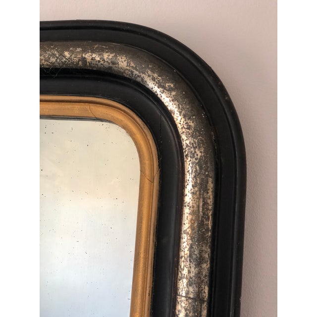An elegant antique French Louis Philippe mirror, dating to the late 19th century. The mirror features a black-painted...