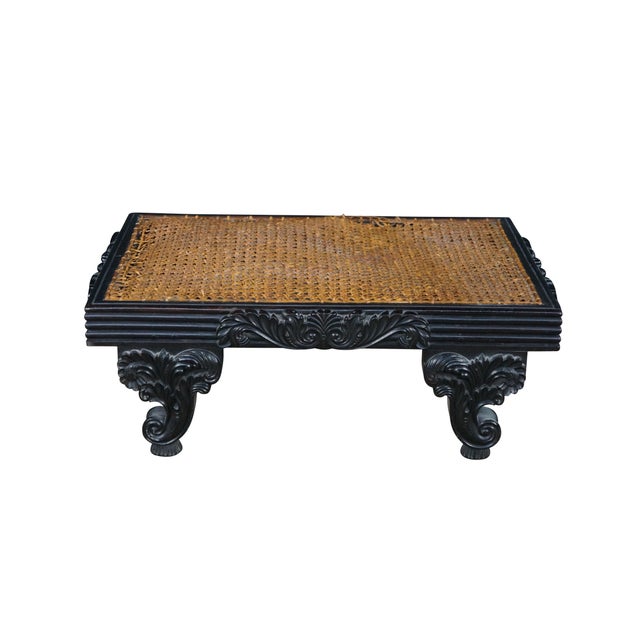 This low-profile rectangular footstool showcases an intricately woven cane top set into a deeply detailed, solid ebony...