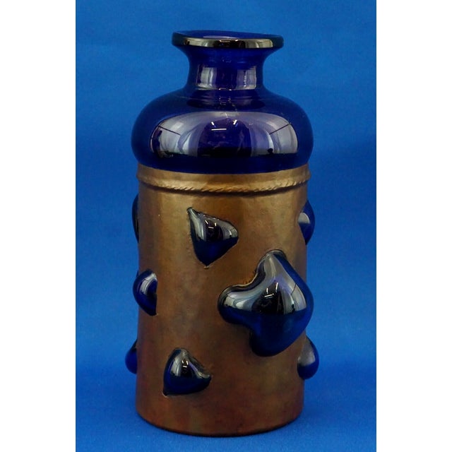 A magnificent blue glass vase with added cobalt oxides, blown into a copper cage. This entirely handcrafted work is...