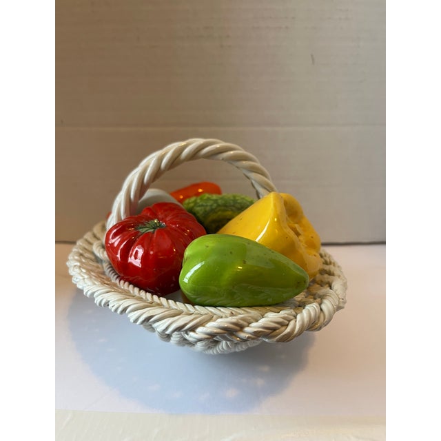 A single vintage porcelain woven basket with handles filled with peppers, onion, broccoli, tomato and carrot.