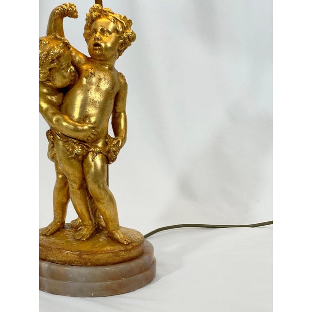 Gilded rococo style putti lamp on pink onyx plinth, Crafted in Italy’s post-war design renaissance, in the 1950s, this...