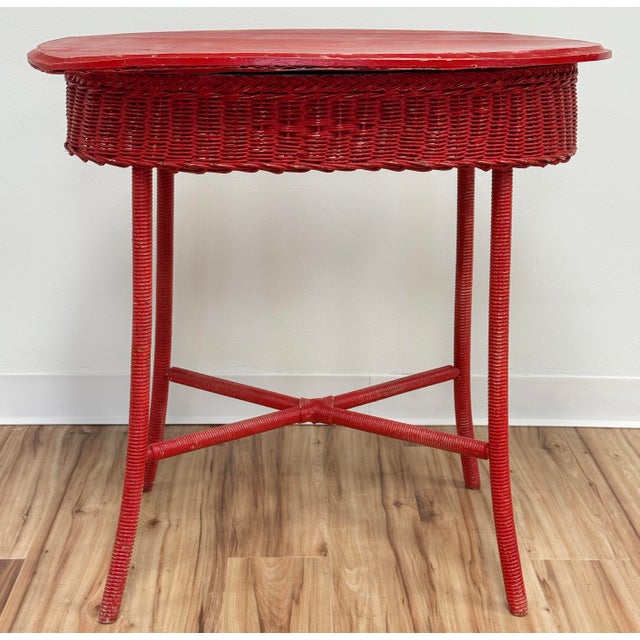 Vintage wicker table with oval slatted wood top in a weathered bold red paint. Four wrapped legs attached by x-base...