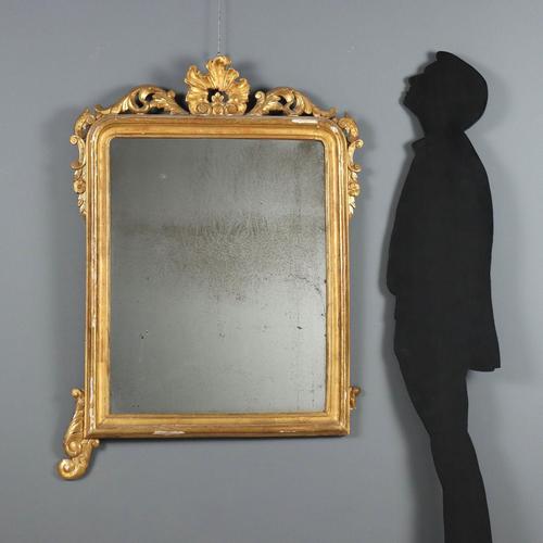 Carved and gilded wooden mirror. The molded frame is enriched with leaf, floral, and scroll carvings on the top and base...