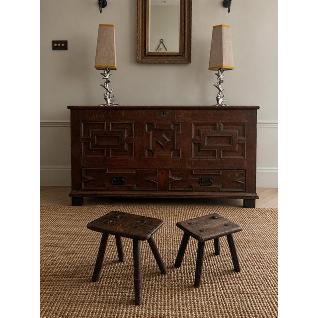 A compact primitive milking stool formed from a single solid hardwood slab with four splayed tapered legs. The wood has a...