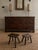 A compact primitive milking stool formed from a single solid hardwood slab with four splayed tapered legs. The wood has a...