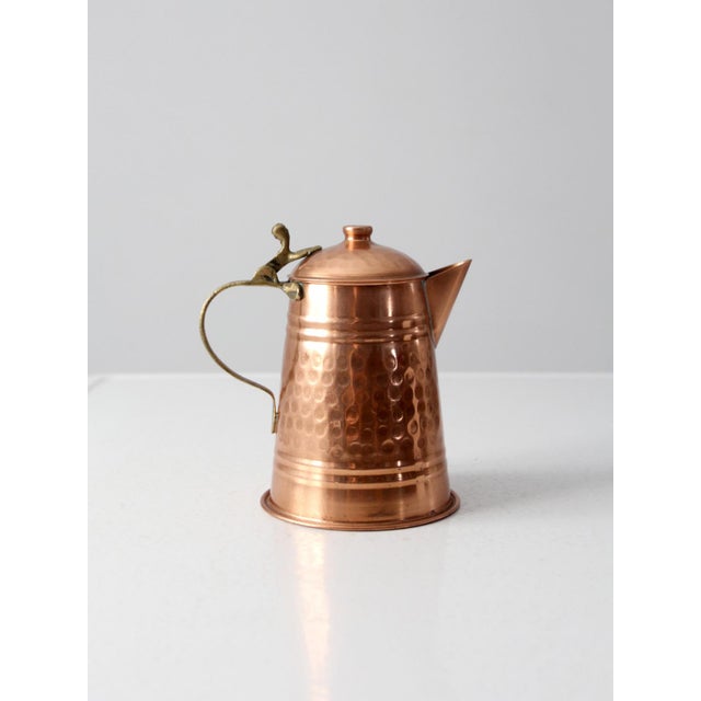 A beautifully crafted vintage teapot in warm hammered copper, accented by an elegant brass handle. Its tapered form, domed...