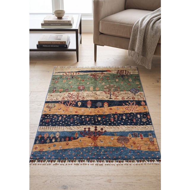 A hand-knotted rug in the Persian Gabbeh style, woven as a layered landscape in sage green, gold, indigo and cream. Hand-...