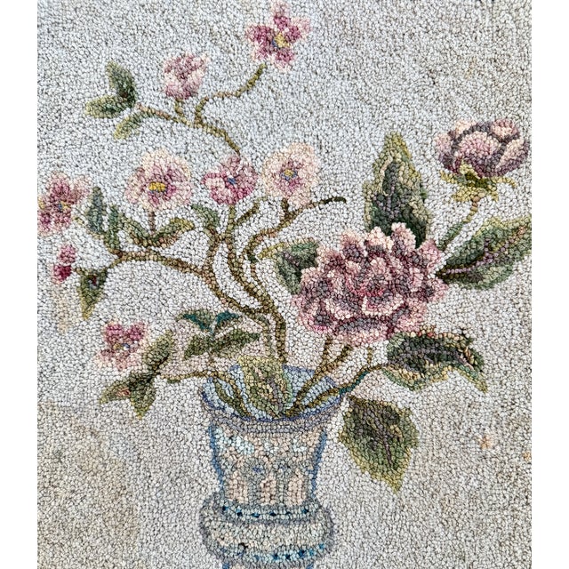 A charming antique hooked rug featuring a softly shaded floral bouquet in a blue and white vase—perfect as a small wall...