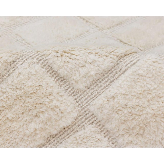 Soft squares of light: a checkerboard sculpted in pure ivory wool. A tone-on-tone checkerboard covers the rug, formed by...