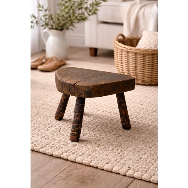 Primitive wooden milking stool with a thick, hand-shaped seat and richly worn patina, supported by three sturdy legs...