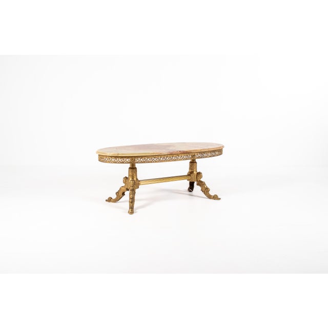 An exceptional vintage Hollywood Regency coffee table featuring a spectacular oval onyx top supported by an ornate gilt...