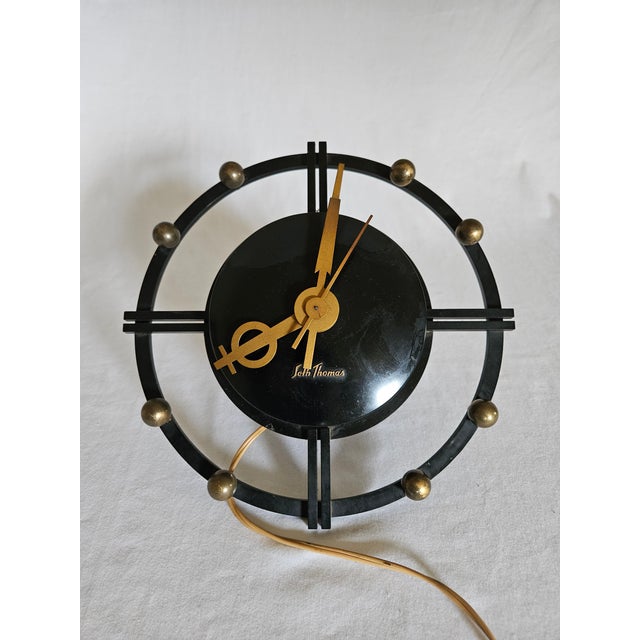 An MCM Atomic design Seth Thomas Electric wall clock. featuring bakalite black body with brass ball hour accents and Brass...