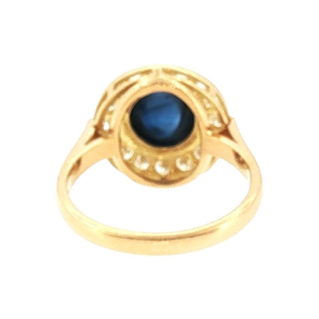 A late 20th-century 18k gold ring featuring a central cabochon-cut blue sapphire, weighing approximately 2.0 carats....
