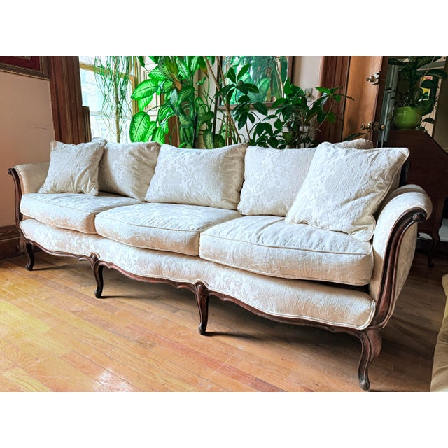 Mid-20th century French Provincial sofa featuring a gently arched scroll back and carved exposed wood frame. The cabriole...