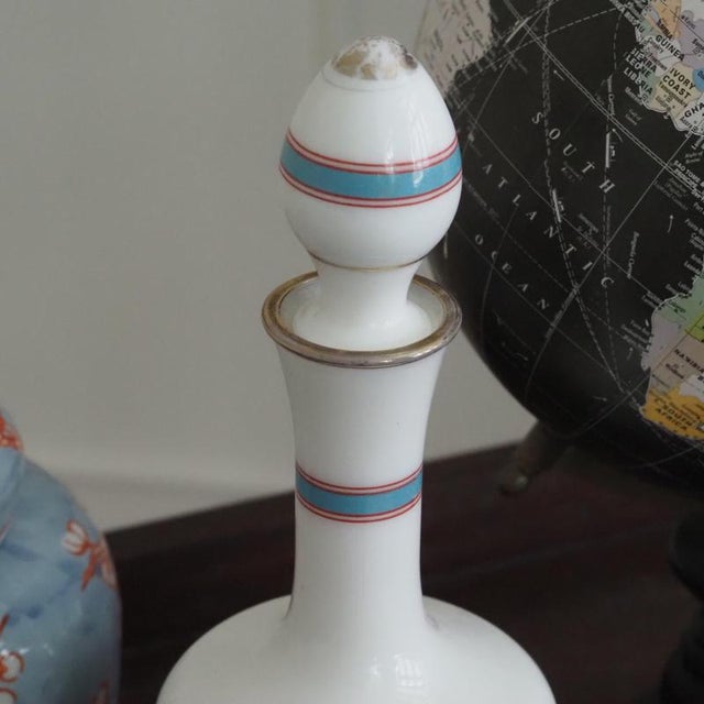Elegant glass carafe in the Neoclassical style with a white background, red medallion, and antique-style head profile....