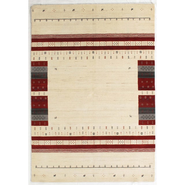 Vintage Hand-knotted Indo Gabbeh rug featuring an open ivory field framed by bold red borders and decorative side panels....