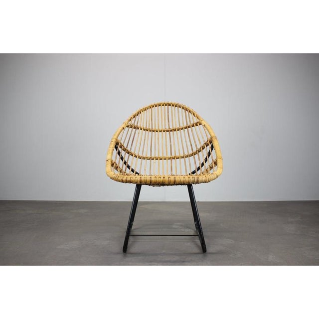 The chair features a sculptural hand-woven natural rattan seat and backrest mounted on a lightweight black-painted tubular...