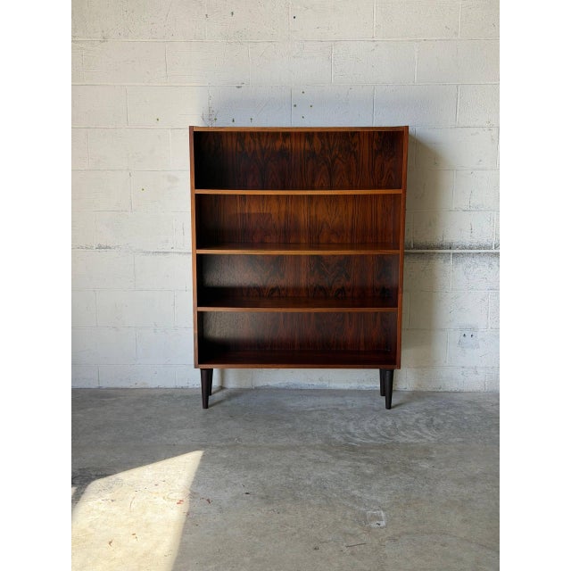 This sleek open shelf bookcase features three spacious tiers for storage and display. Elevated on dark tapered legs, it...