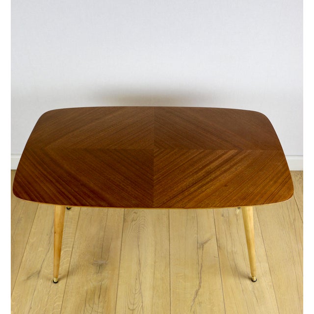 A rounded, rectangular wooden coffee table from the 1970s, beautifully crafted on round, twisted legs with gold feet. The...