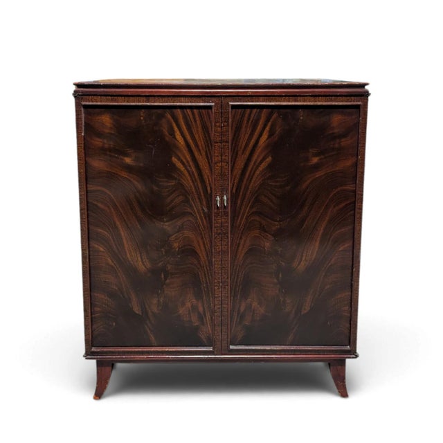 A vintage two-door storage cabinet with dramatic, mirror-matched flame-pattern mahogany veneers. Framed door panels, a...