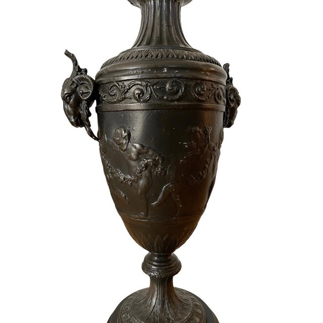 A 1940s neoclassical style black spelter urn standing 22" tall and featuring cherub figures holding hands around the body...