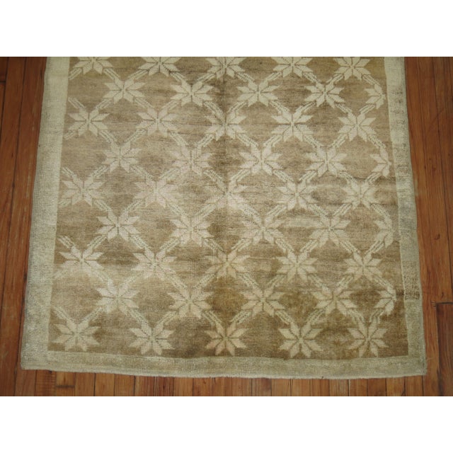 A wide turkish gallery size rug in with a repetitive star motif on a soft brown field surrounded by a narrow green gray...