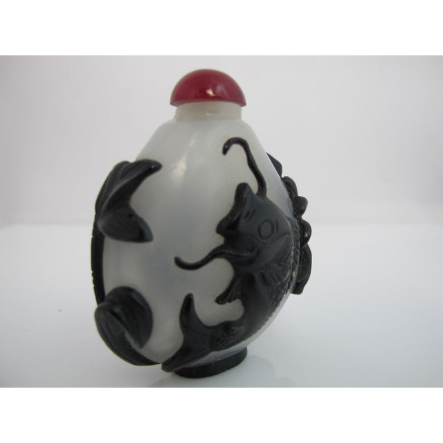 Chinese glass snuff bottle with carved koi fish and foliage design in black. Translucent glass with red stopper. Excellent...