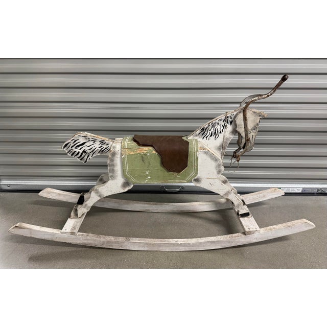 Antique wooden rocking horse, likely dating from the late 19th century or early 20th century. The rocking horse features a...