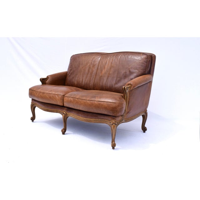 A vintage leather loveseat with rolled form carved arms, brass nail head trim and loose seat cushions supported on...