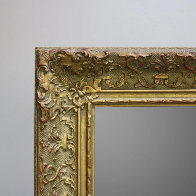 An antique and large Continental giltwood wall mirror offers frame with scroll foliate and stylized fleur-de-lis...