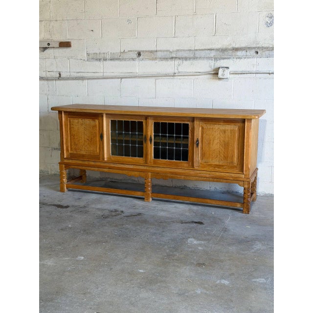 This architectural low console features a long rectilinear frame with a central pair of leaded glass doors. The balanced...