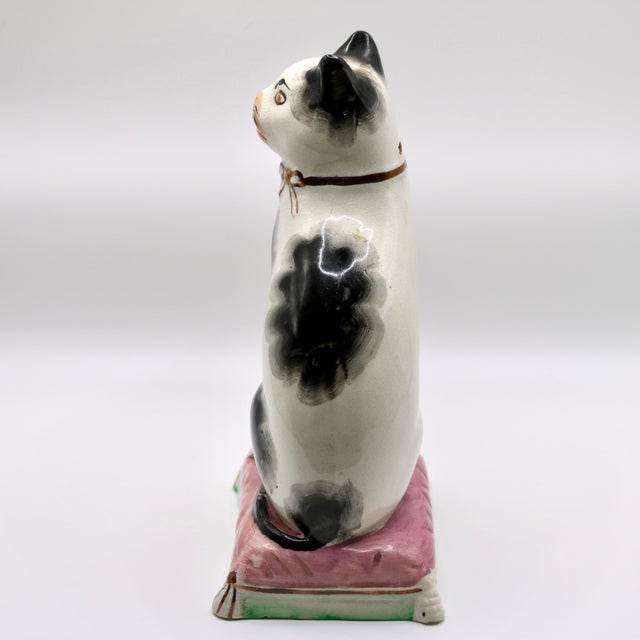 A charming 19th-century antique English Staffordshire pottery mantel figurine depicting a seated black and white cat....