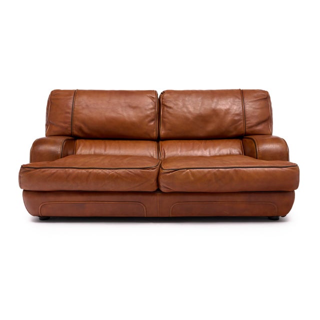 A handsome Italian two-seat sofa from the 1970s, upholstered in beautifully aged cognac leather with a rich, warm patina....