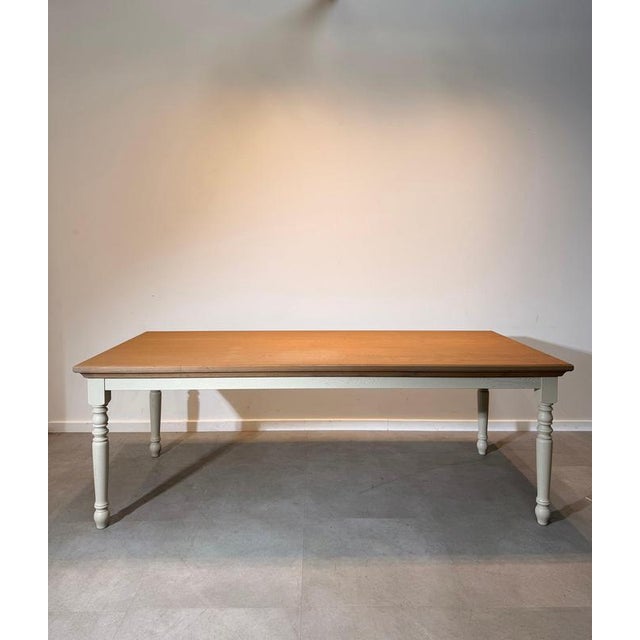 Elegant dining table combining a warm natural oak top with contrasting painted turned legs. The solid proportions,...