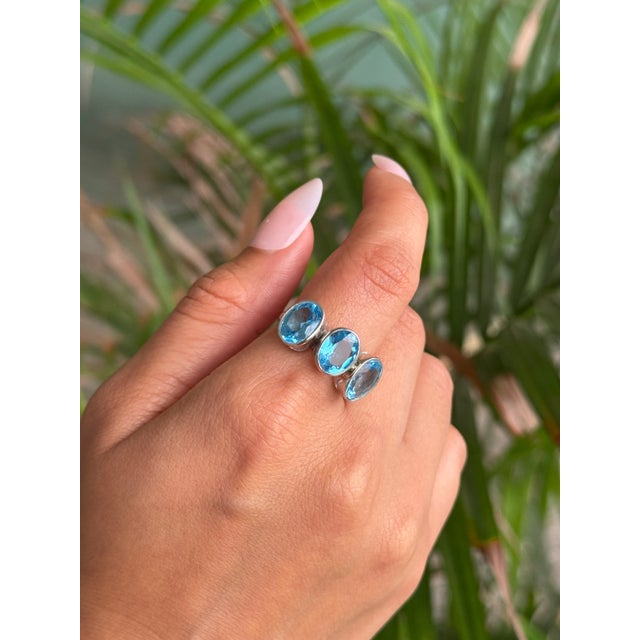 Crafted in 925 Sterling Silver, this elegant ring features three oval-cut Blue Topaz gemstones, radiating a serene ocean-...