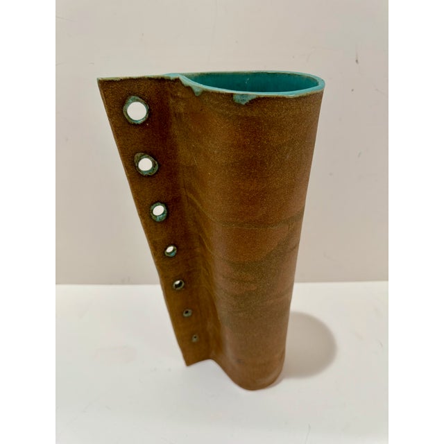 Sculptural vintage ceramic vase with tall cylindrical form, warm brown glaze, and a vertical row of pierced openings with...