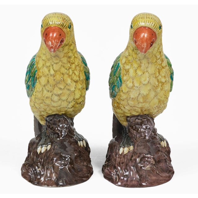 Pair of colorful Chinese antique yellow and green feathered parrots with orange beaks standing on a brown tree stump.