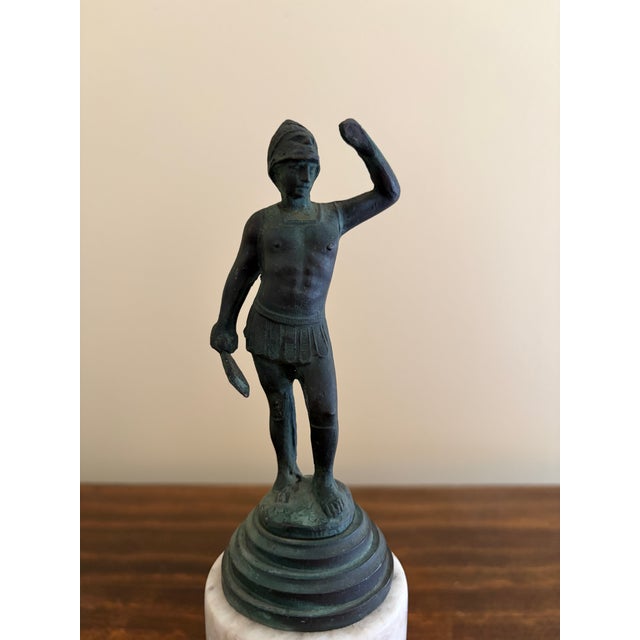 A Grand Tour–style classical figure in brass, mounted on a cylindrical marble base. The slightly more relaxed posture and...