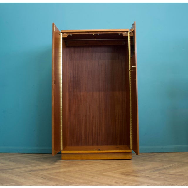 A clean mid-century two-door wardrobe in walnut, with a warm tone and simple grain. Integrated oval handles. Standing on a...