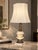 Ornate table lamp with a cream/ivory glass globe body, a gold-tone floral band, a cherub detail and an intricately cast...