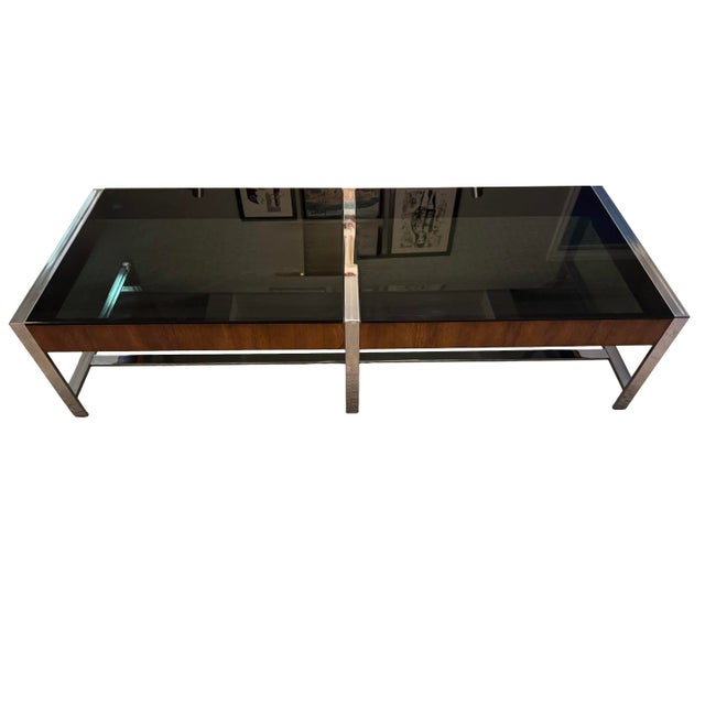 Large mid-century modern coffee table featuring a polished chrome frame, smoked glass top, and warm walnut-tone wood...