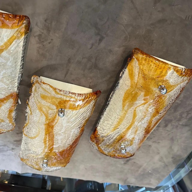 This is a set of four Mid-Century Modern white, amber and brown Murano glass wall sconces, crafted by Mazzega in the...