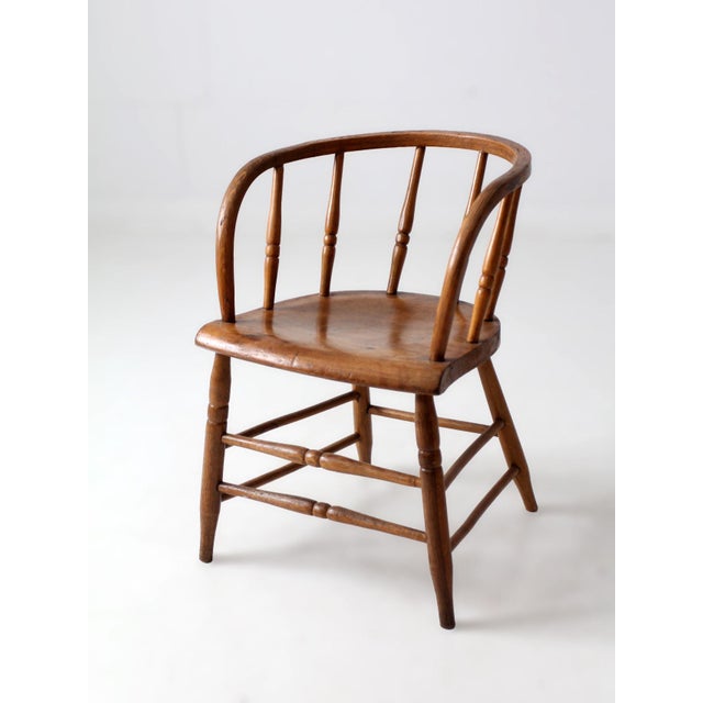 A late 1800s Windsor captain’s chair with a graceful wraparound back, turned spindles, shaped wood seat, and stretcher...