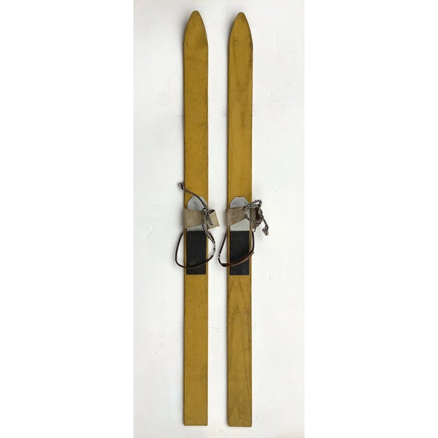 Vintage pair of children's wood skis in original yellow paint, bindings are rubber and metal with leather straps. Skis...