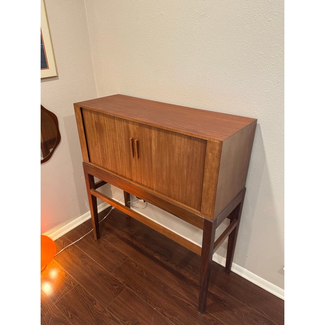 A tall mid century modern Danish cocktail cabinet with tambour doors, circa 1960s. Beautifully crafted in teak with an...